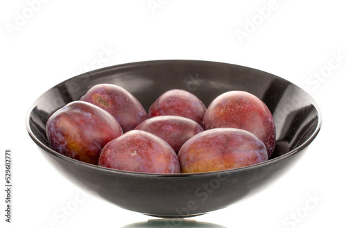 Several juicy plums on a ceramic black plate  macro  isolated on a white background.