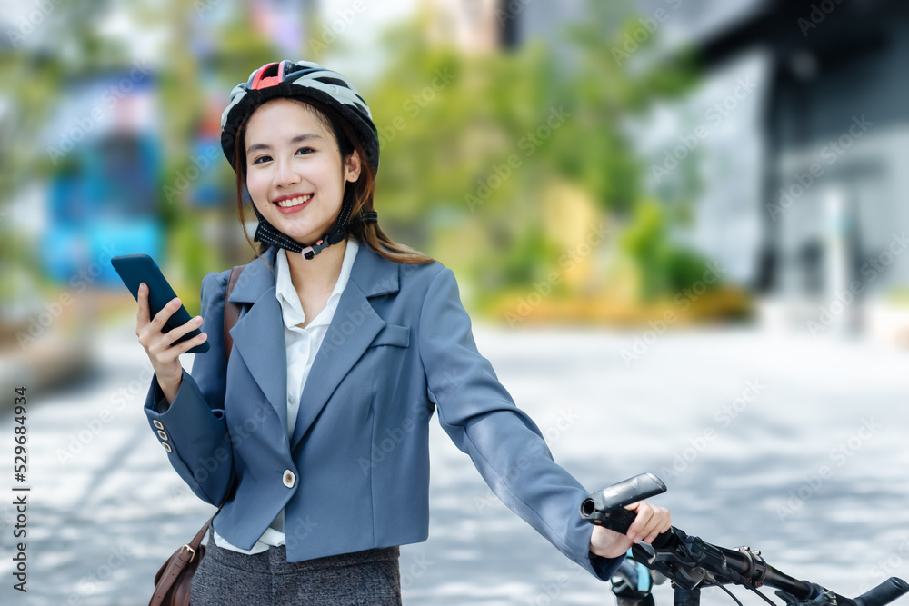 Young Asian businesswoman wearing helmet and standing on a city street with bicycle looking at phone.