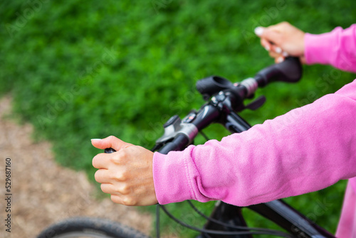 A girl in a pink sweatshirt holds on to the handlebars of a bicycle, a bike ride in the park. Outdoor recreation is good for health.