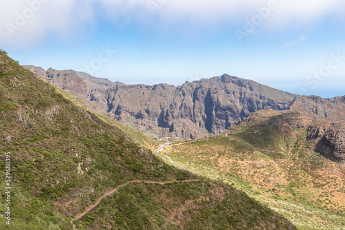 Panoramic view on scenic hiking trail over lush green hill in Teno mountain range, Tenerife, Canary Islands, Spain, Europe. Path leads to remote village Masca. Moody mystical vibes on tropical island