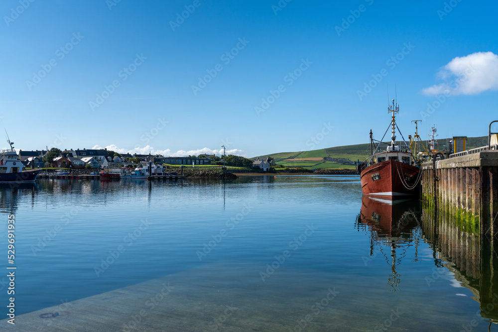 Fototapeta premium red fishing boat on the docks of Dingle Harbor in County Kerry with reflections in the calm water