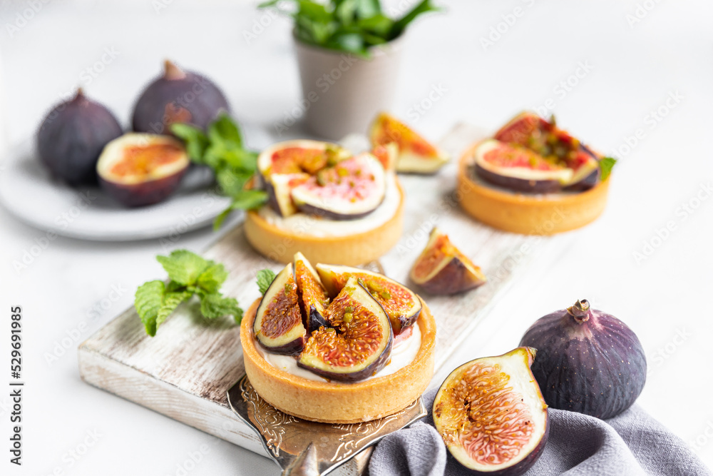Tartlets with delicate cream cheese and fresh figs decorated with mint and pistachio, light gray background. Autumn dessert. National Dessert Day, October 14. Tartlets with delicate cream cheese and fresh figs decorated with mint and pistachio, light gray background. Autumn dessert. National Dessert Day, October 14.