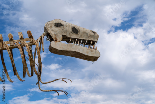 T-Rex dinosaur skeleton against a partly cloudy blue sky photo