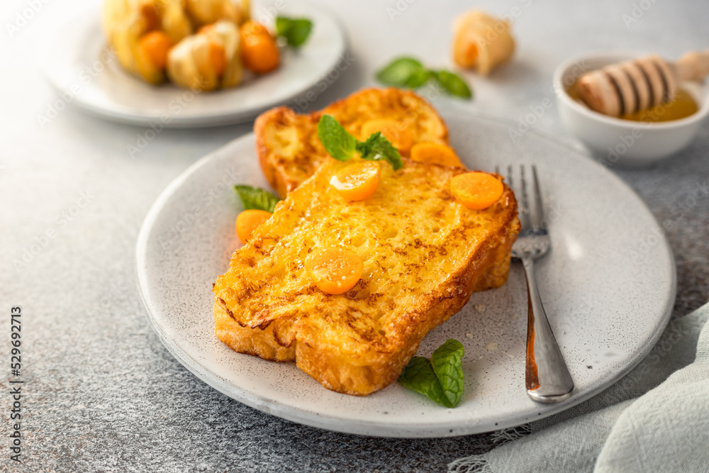French brioche toast with physalis, honey and mint on ceramic plate, grey background. Traditional sweet breakfast with fried bread with egg and milk. French brioche toast with physalis, honey and mint on ceramic plate, grey background. Traditional sweet breakfast with fried bread with egg and milk.