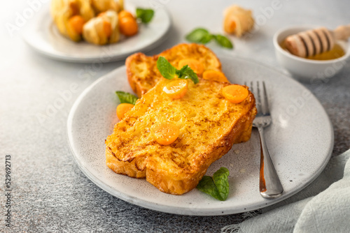 French brioche toast with physalis, honey and mint on ceramic plate, grey background. Traditional sweet breakfast with fried bread with egg and milk.
