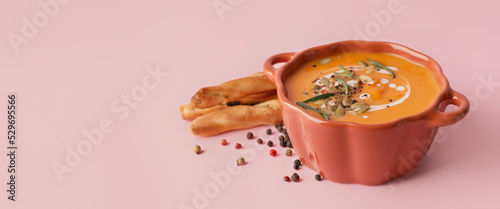 Tasty pumpkin cream soup in pot on pink background with space for text