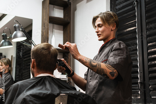 Stylish woman barber cutting hair to man in salon