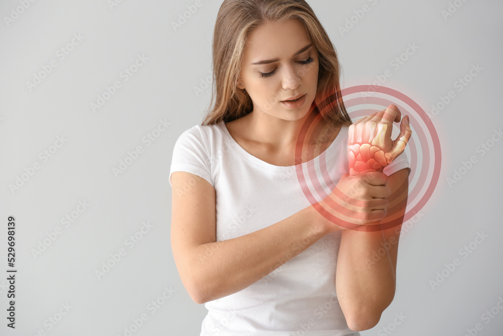 Young woman with pain in wrist on light background Young woman with pain in wrist on light background