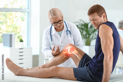 Mature doctor giving sporty man with joint pain injection in clinic photo