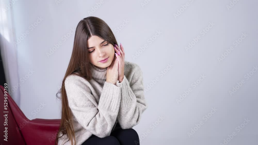 Beautiful long-haired young lady sitting in armchair indoors. Attractive woman bent her head looking down. White backdrop. Beautiful long-haired young lady sitting in armchair indoors. Attractive woman bent her head looking down. White backdrop.