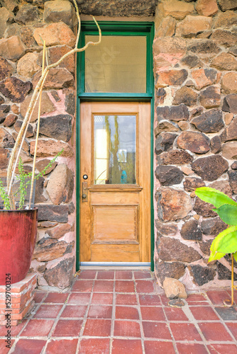 Wooden front door with glass panel and transom window in between a rockwall at Tucson, AZ