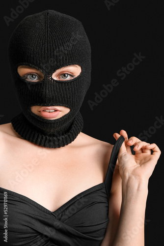 Portrait of young woman in balaclava on black background