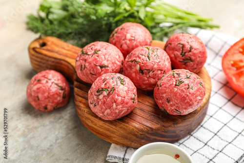 Cutting board with raw meat balls, herbs and napkin on grunge background