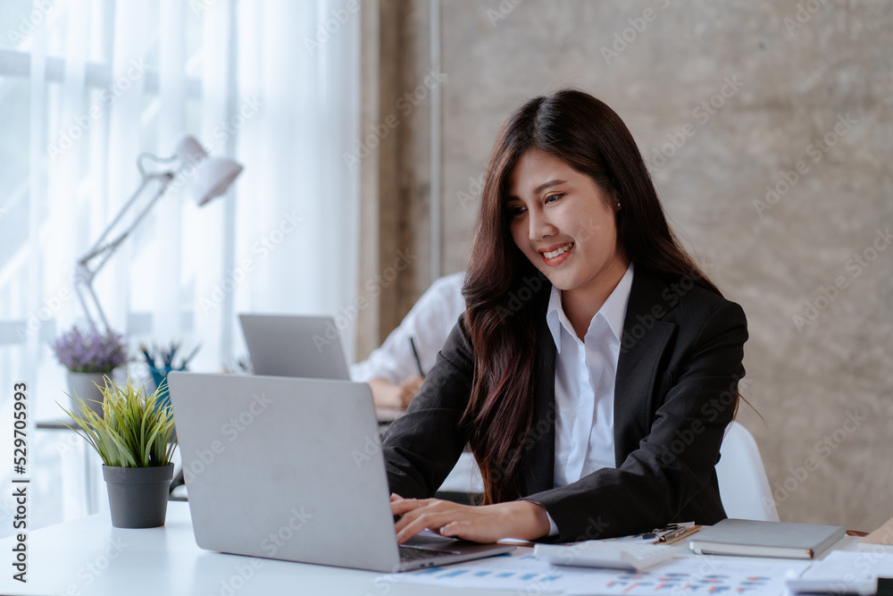 Happy young Asian businesswoman sitting on her workplace in the office. Young woman working at laptop computer in the office Happy young Asian businesswoman sitting on her workplace in the office. Young woman working at laptop computer in the office