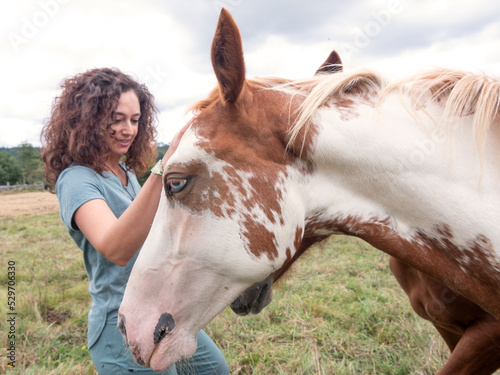 Side view of brunette woman stroking an american paint horse.