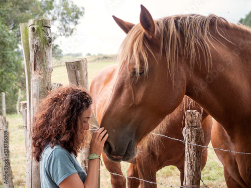 Brunette woman forming bond with a Hispano-Breton horse behind a barb wire fence in a field.