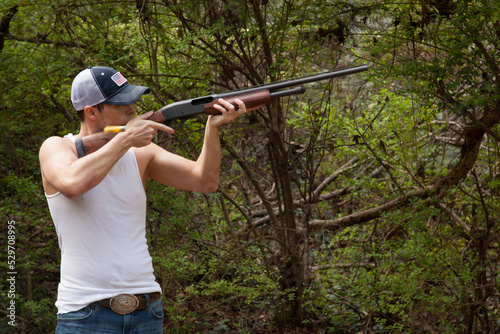 Man in an undershirt outside with a shotgun
