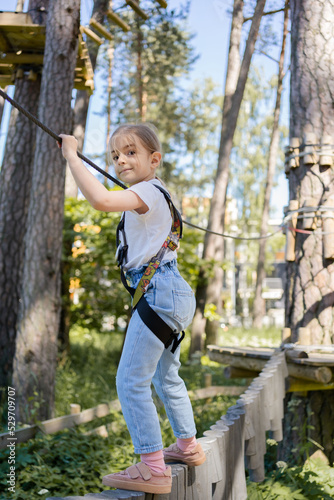 Kid passing the cable route high among trees. Child climbing in high rope course in adventure park. Children in forest rope park. 