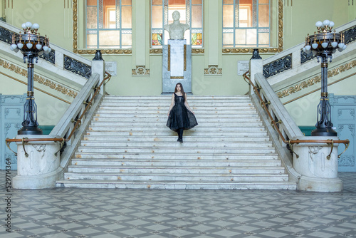 Beautiful girl in black dress running down wide stairs in hall checkered floor. High quality photo