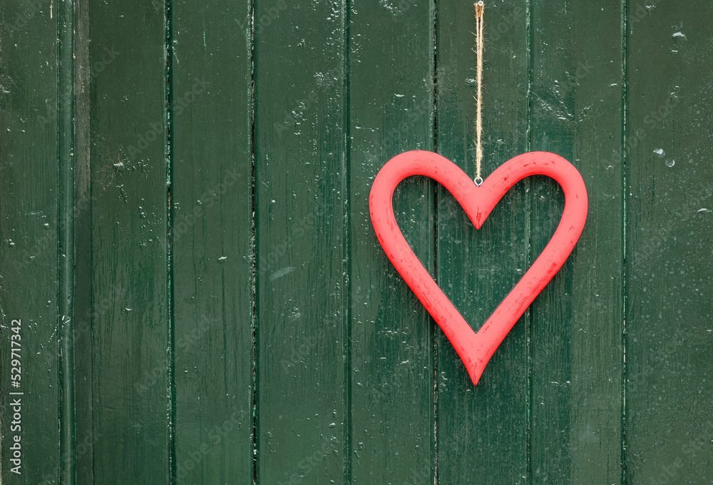 red heart shape hanging in front of a textured green door, close up, love concept red heart shape hanging in front of a textured green door, close up, love concept