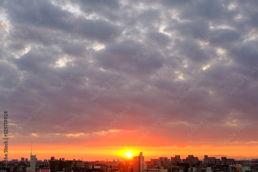 都市の夜明け。日の出とともに空と雲がオレンジ色に染まり、ビル群はシルエットとして写す神戸市街地から芦屋、大阪方面を臨む