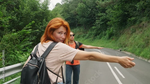 Women with backpacks try to catch car walking on forest road photo