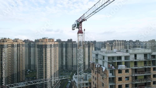 Aerial view of a construct residential high-rise buildings, cranes, steel, concrete, cargo, work next to park and highway in the St. Petersburg at sunny summer afternoon, shadows, horizon