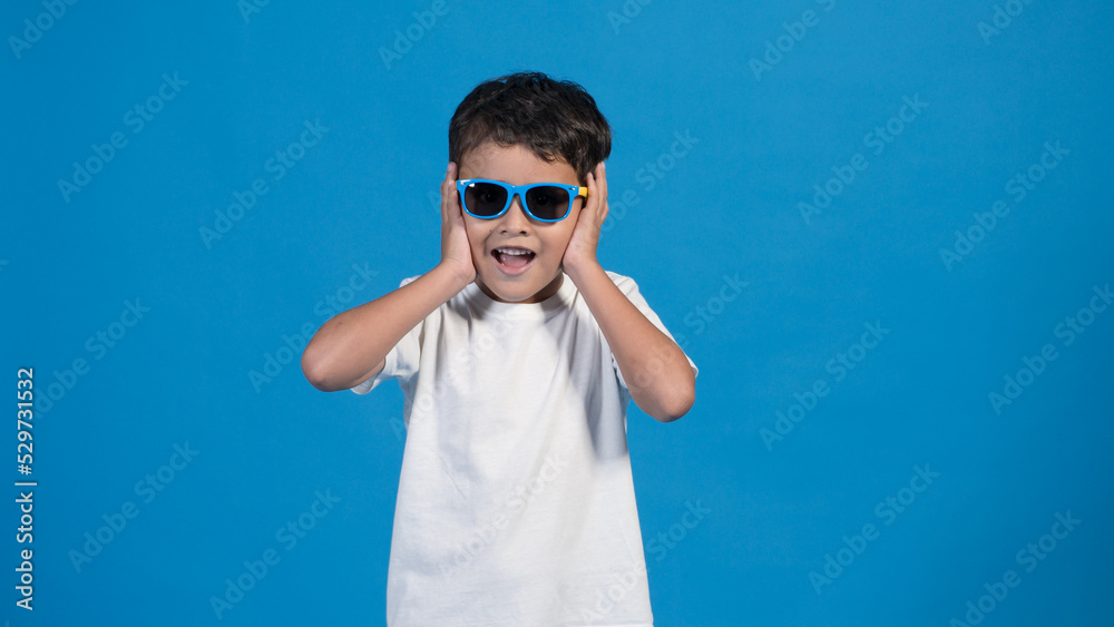 Hermoso niño con playera blanca y fondo azul. Usando lentes y tocando su cara Hermoso niño con playera blanca y fondo azul. Usando lentes y tocando su cara