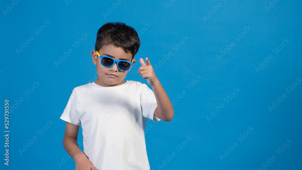 Hermoso niño con playera blanca y fondo azul. Usando lentes y señalando con su dedo. Hermoso niño con playera blanca y fondo azul. Usando lentes y señalando con su dedo.