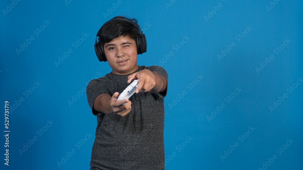 Retrato de estudio de un niño jugando a videojuegos con auriculares y joystick. fondo Azul.