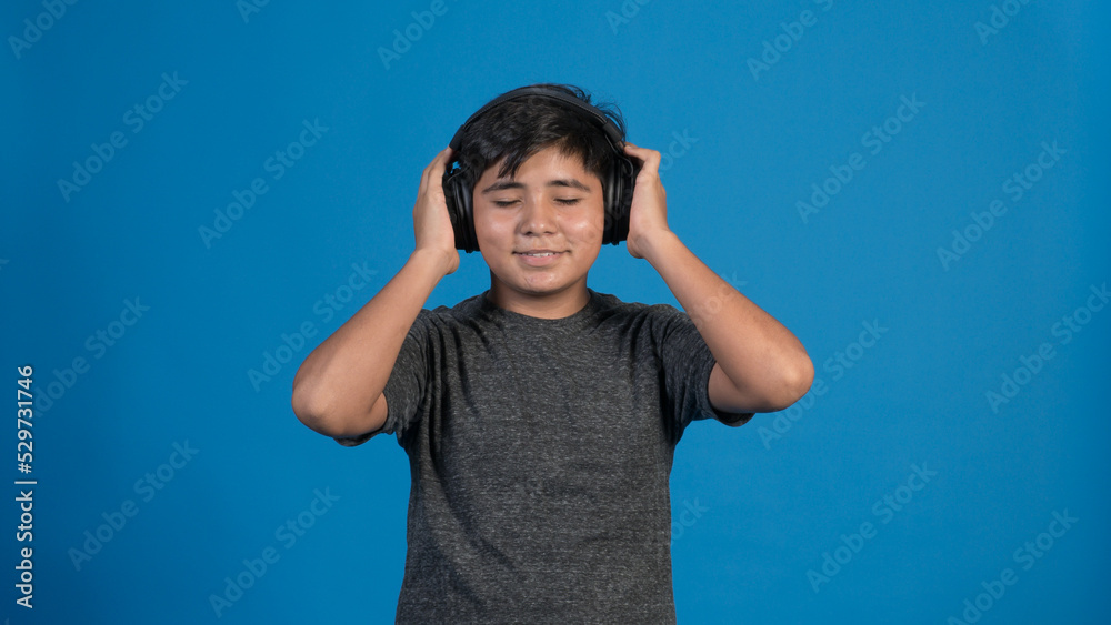 Retrato de estudio de un niño escuchando música tocando con sus manos los audífonos. Con fondo Azul