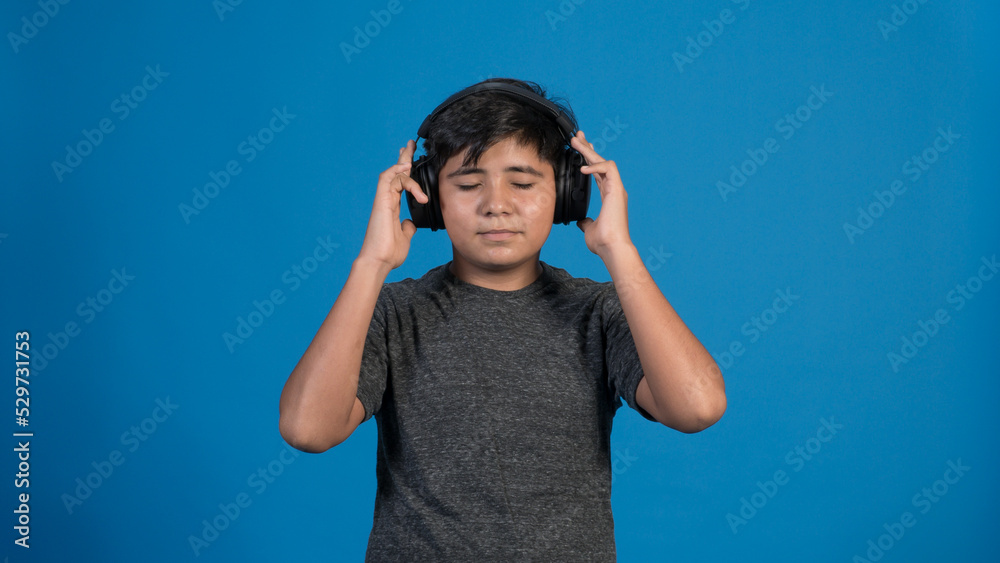 Retrato de estudio de un niño escuchando música tocando con sus manos los audífonos. Con fondo Azul Retrato de estudio de un niño escuchando música tocando con sus manos los audífonos. Con fondo Azul