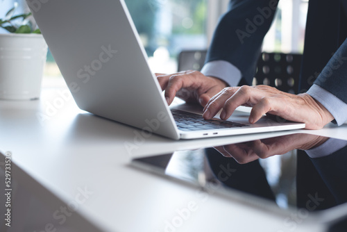 Businessman hands typing, working on laptop computer with digital tablet on white office table. Man manager surfing the internet, searching the information
