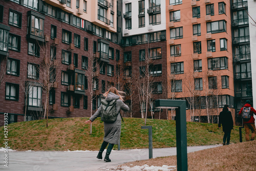 Back view of a woman in a jacket and backpack running in the modern residential building. College. Student. University. Trendy. Happiness. Walking. Walk. Vitality. Vacations. Daytime. Energy. Motion. © AndriiKoval