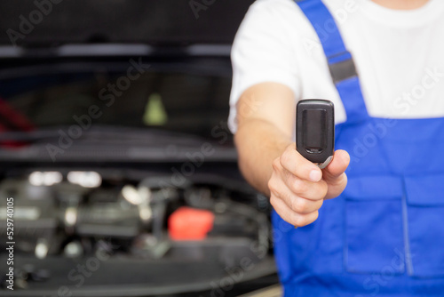 Closeup hands of mechanic giving key after repair car at garage, auto service, insurance with satisfaction to client, maintenance and fix of vehicle, transportation and industrial concept.