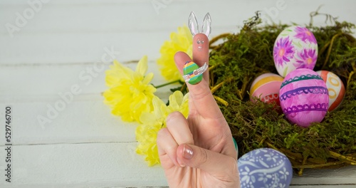 Cropped hand with creative bunny cartoon drawing on crossed fingers over easter eggs in nest