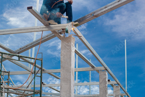 Male worker use metal cutting spark or Oxyfuel Gas cutting on steel roof truss with flash on blue sky background in construction site. photo