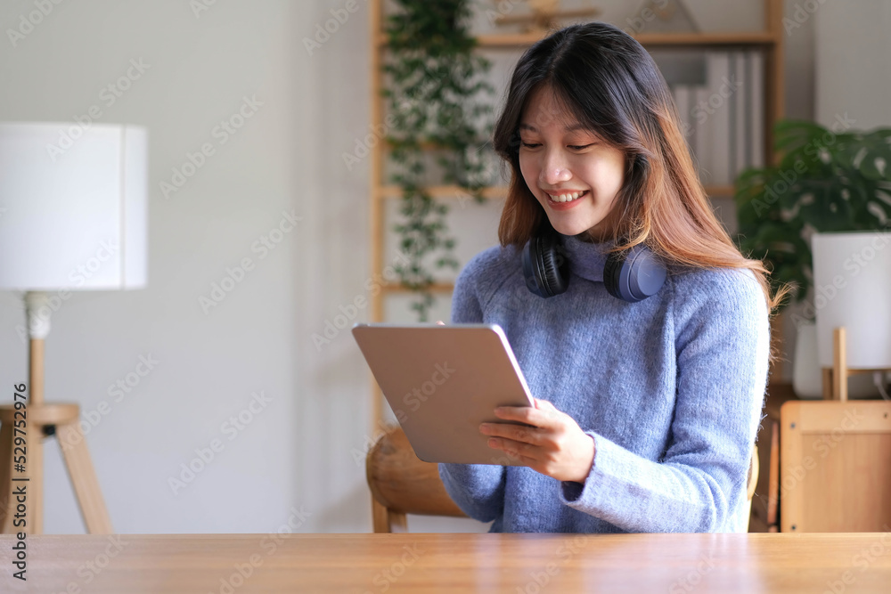 Portrait of smiling happy beautiful asian woman relaxing using technology of tablet while sitting on table.Young creative girl working and typing on keyboard at home.work at home concept Portrait of smiling happy beautiful asian woman relaxing using technology of tablet while sitting on table.Young creative girl working and typing on keyboard at home.work at home concept