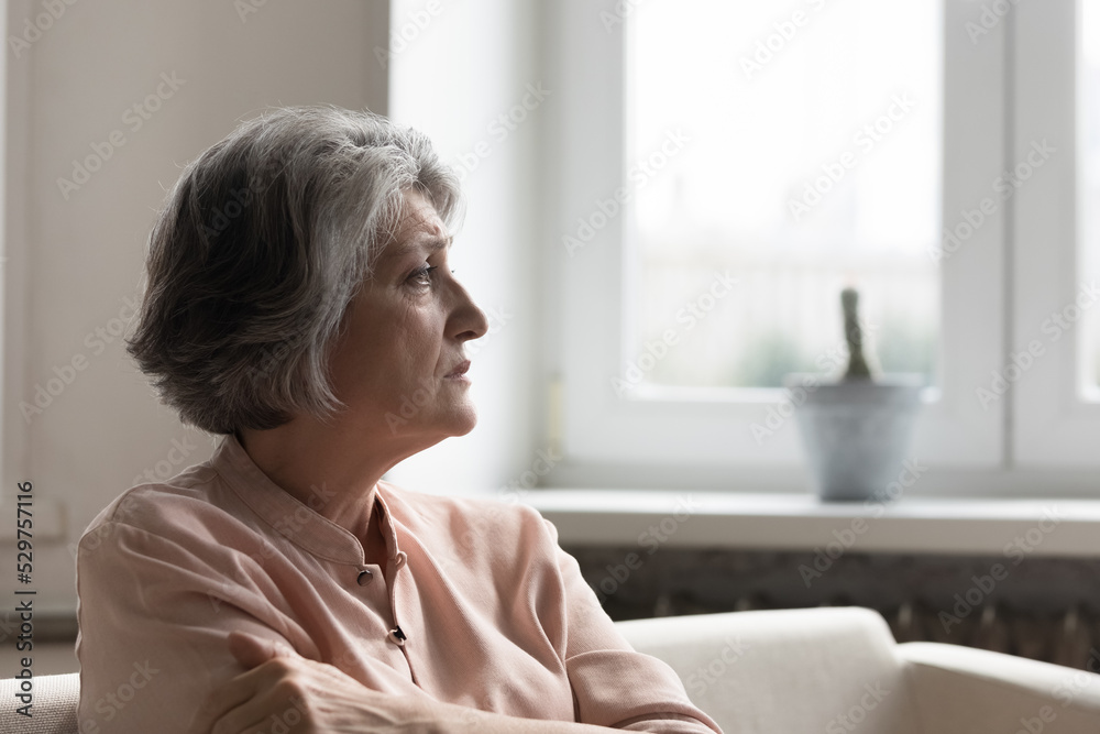 Concerned anxious senior 60s woman looking away, sitting on couch at home, thinking over problems, feeling depressed, worried, frustrated, facing loneliness, loss, grief, disease, mental disorder - obrazy, fototapety, plakaty 