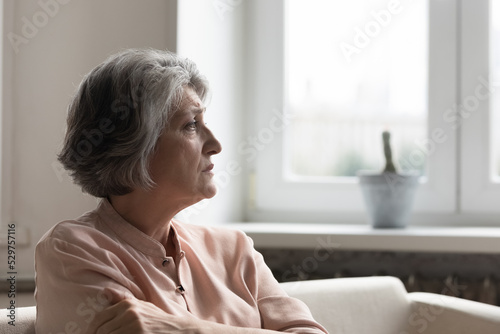 Obraz na plátně Concerned anxious senior 60s woman looking away, sitting on couch at home, think