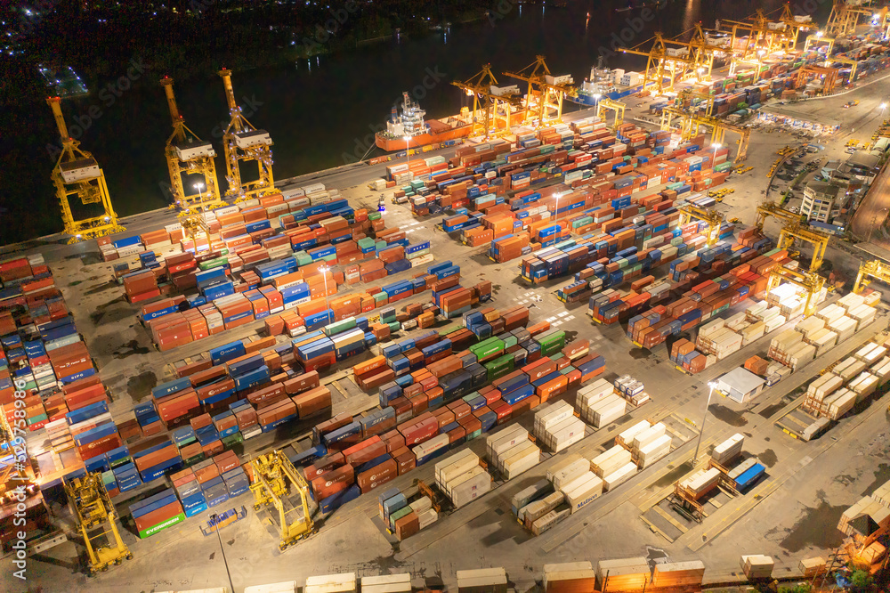 Fototapeta premium Aerial view of container cargo ship in the export and import business and logistics international goods in urban city. Shipping to the harbour by crane in Bangkok harbour, Thailand at night.