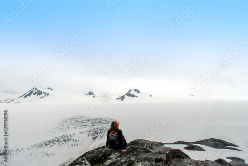 Female hiker sitting on the top of a mountain summit looking out over the Harding Ice Field in Alaska savoring the incredible vistas and surreal views of Nunataks and snow covered mountains. photo