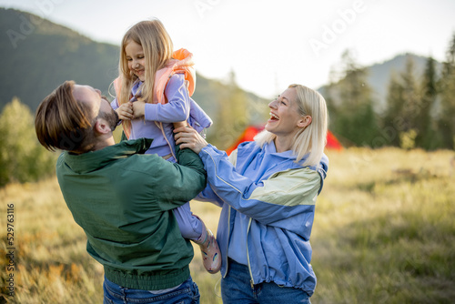 Young caucasian couple with little girl and dog have fun while hiking in the mountains. Happy family spend summer vacation at campsite. Father tossing daughter in his arms photo