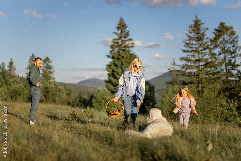 Young caucasian couple with little girl and dog have fun spending leisure time together on nature. Happy family traveling in the mountains