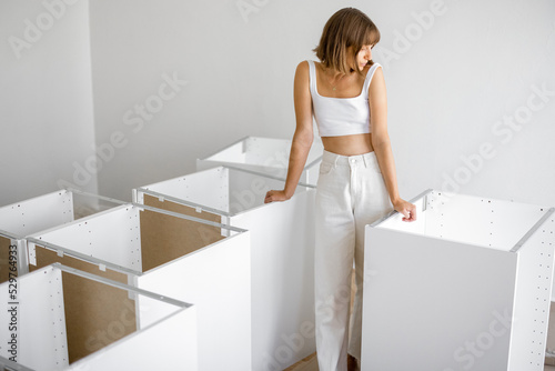 Portrait of a young cheerful housewife stands with new furniture in apartment. Woman in white clothes during home improvement
