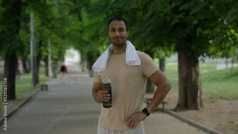 Portrait of the afro american man looking at the camera holding sport bottle wearing smart watch carries a towel around his neck in the park after the training. Sport and healthy lifestyle concept. Portrait of the afro american man looking at the camera holding sport bottle wearing smart watch carries a towel around his neck in the park after the training. Sport and healthy lifestyle concept.