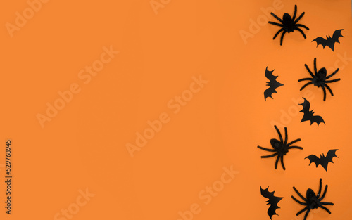Halloween Background with Black Spiders and Bats. Big Black Hairy Spiders and Little Flying Bats on an Orange Background. Halloween Flat Lay. Top View Composition ideal for Banner, Flyer. © Magdalena