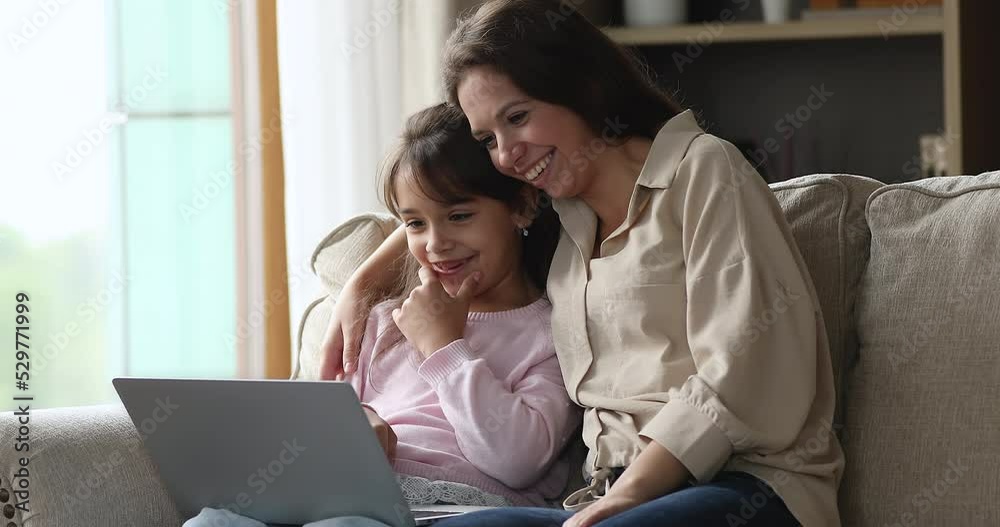 Cheerful mom and sweet little daughter kid watching, commenting, discussing cartoon movie on laptop, using computer for video call, speking, talking, smiling, laughing