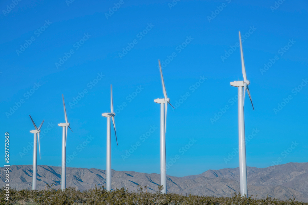 White tubular wind turbines against the mountain range and blue sky in California White tubular wind turbines against the mountain range and blue sky in California