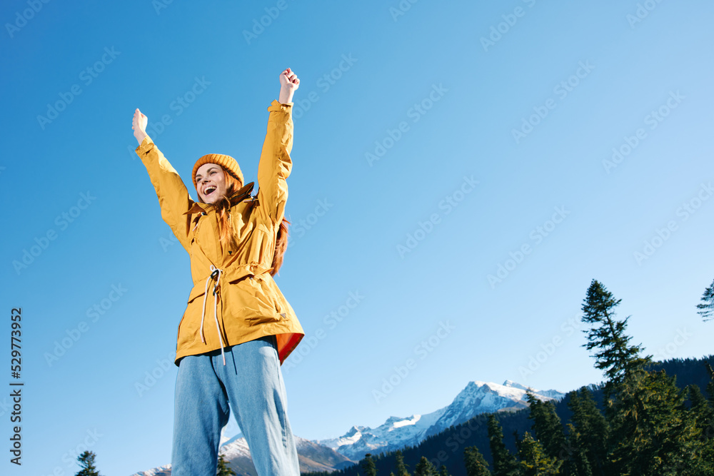 Woman with red hair hiker in yellow raincoat and cap standing on the mountain hands up happiness with a view of snowy mountains travel in winter and hiking in the mountains in the sunset freedom Woman with red hair hiker in yellow raincoat and cap standing on the mountain hands up happiness with a view of snowy mountains travel in winter and hiking in the mountains in the sunset freedom